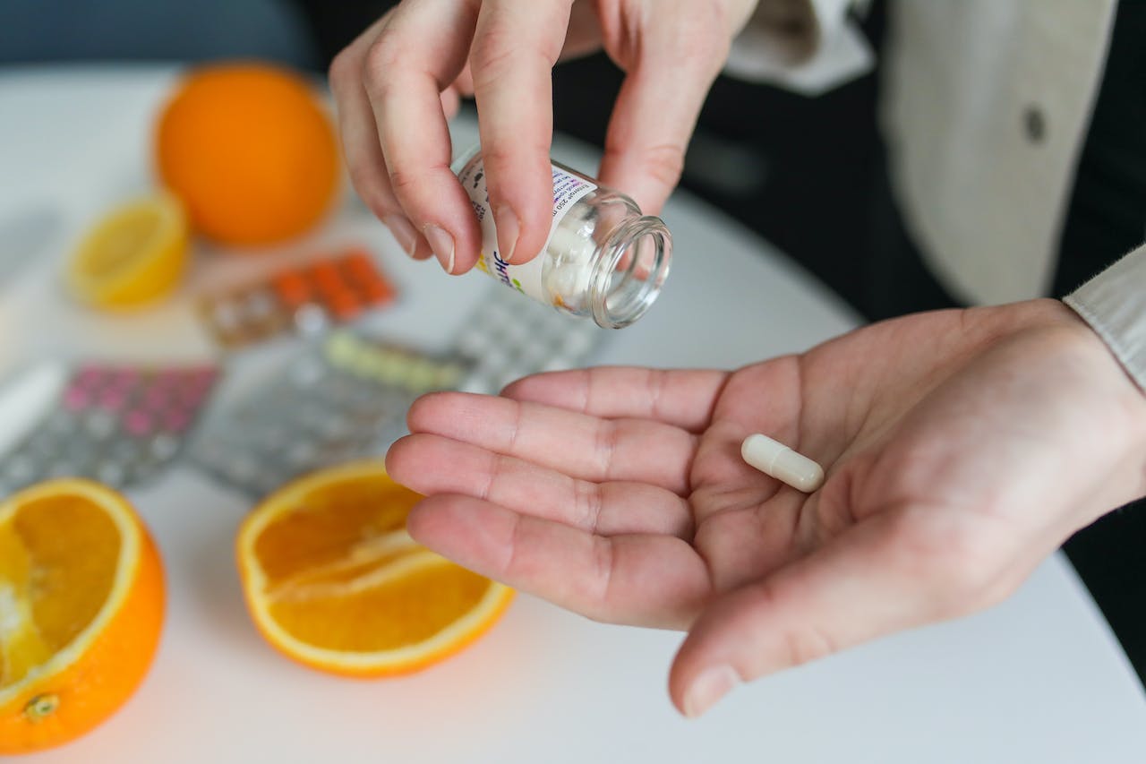 Hand taking vitamin supplement with oranges and cut citrus fruits nearby