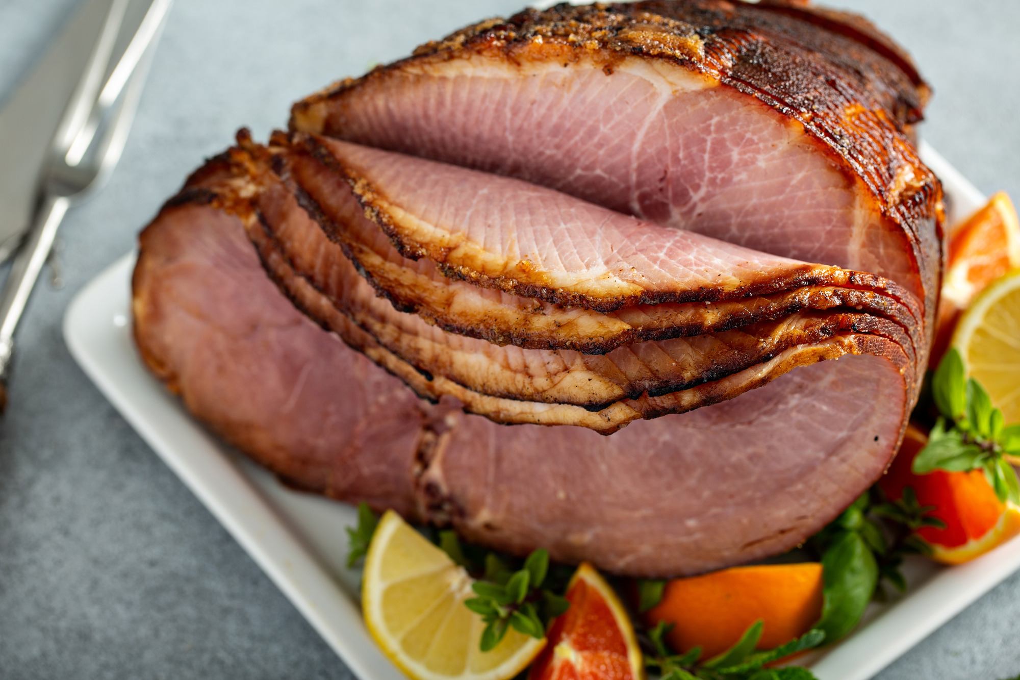 Glazed holiday ham with caramelized crust, served with citrus and herbs