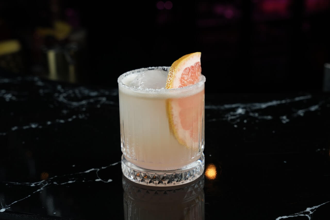 Creamy cocktail with grapefruit garnish on sugar-rimmed glass