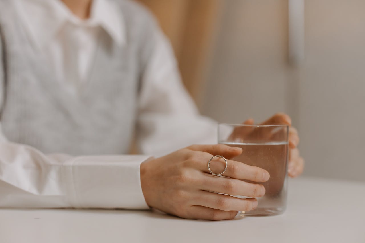 Hand wearing ring holds clear glass on minimalist white table