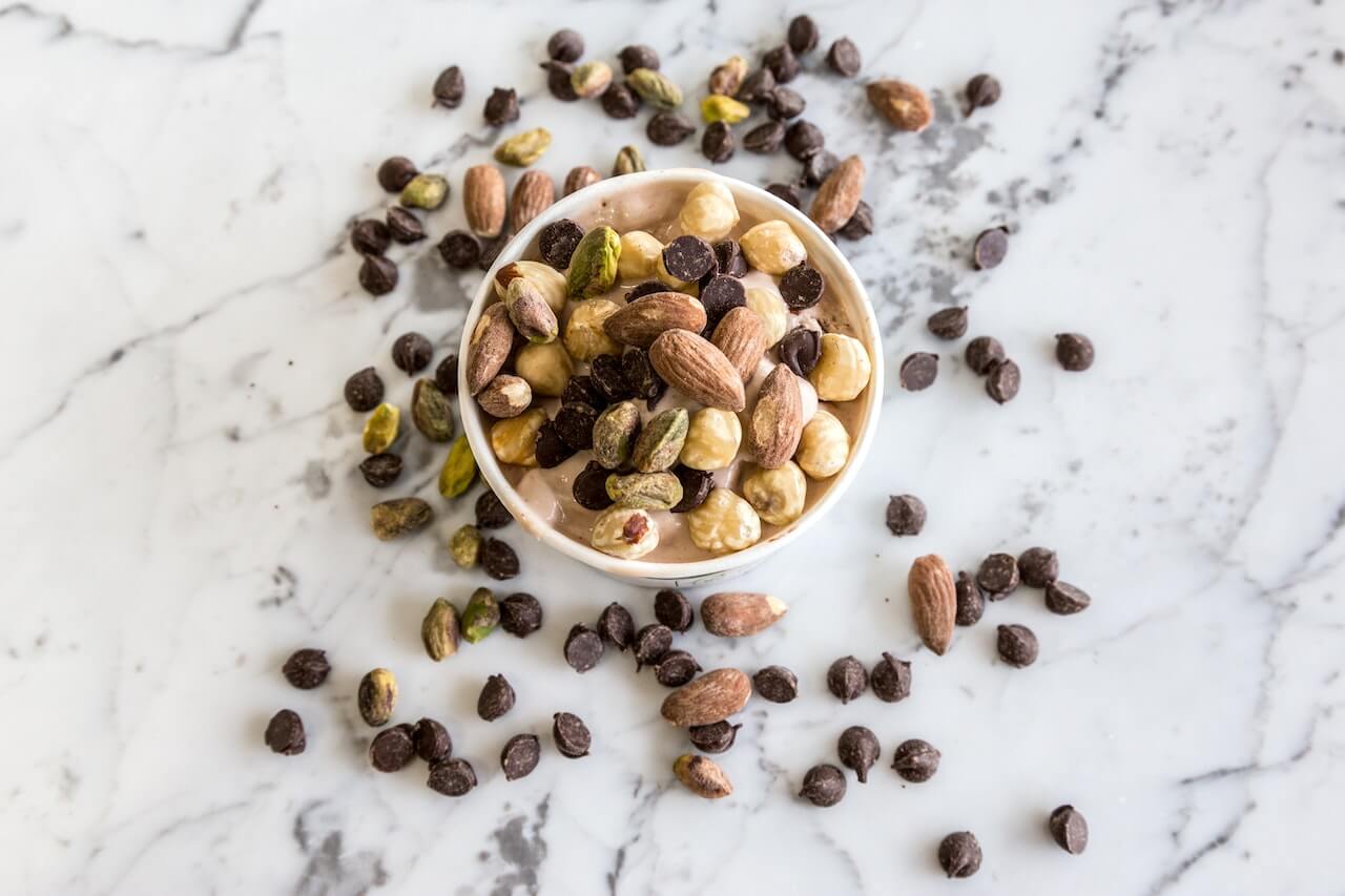 Mixed nuts and chocolate chips scattered on marble surface in white bowl