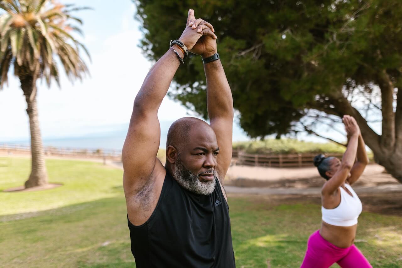 Two people stretching outdoors with palm trees and ocean in background