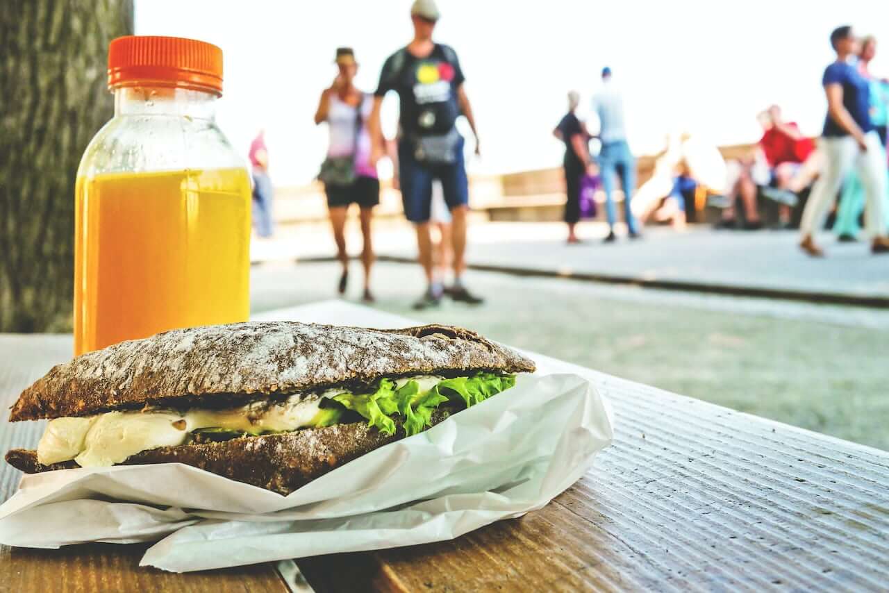 Rustic sandwich with cheese and lettuce next to orange juice bottle