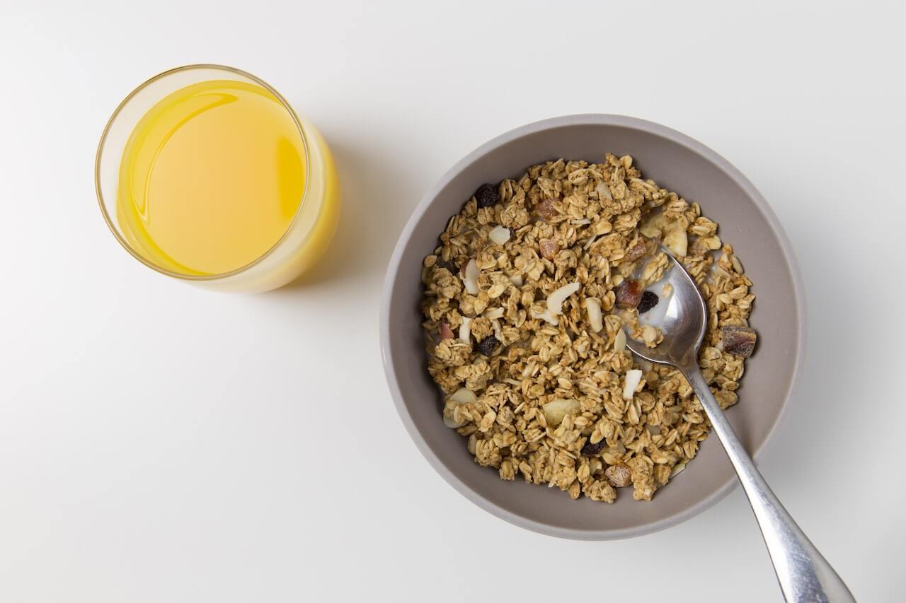 Granola in a gray bowl with orange juice, viewed from above