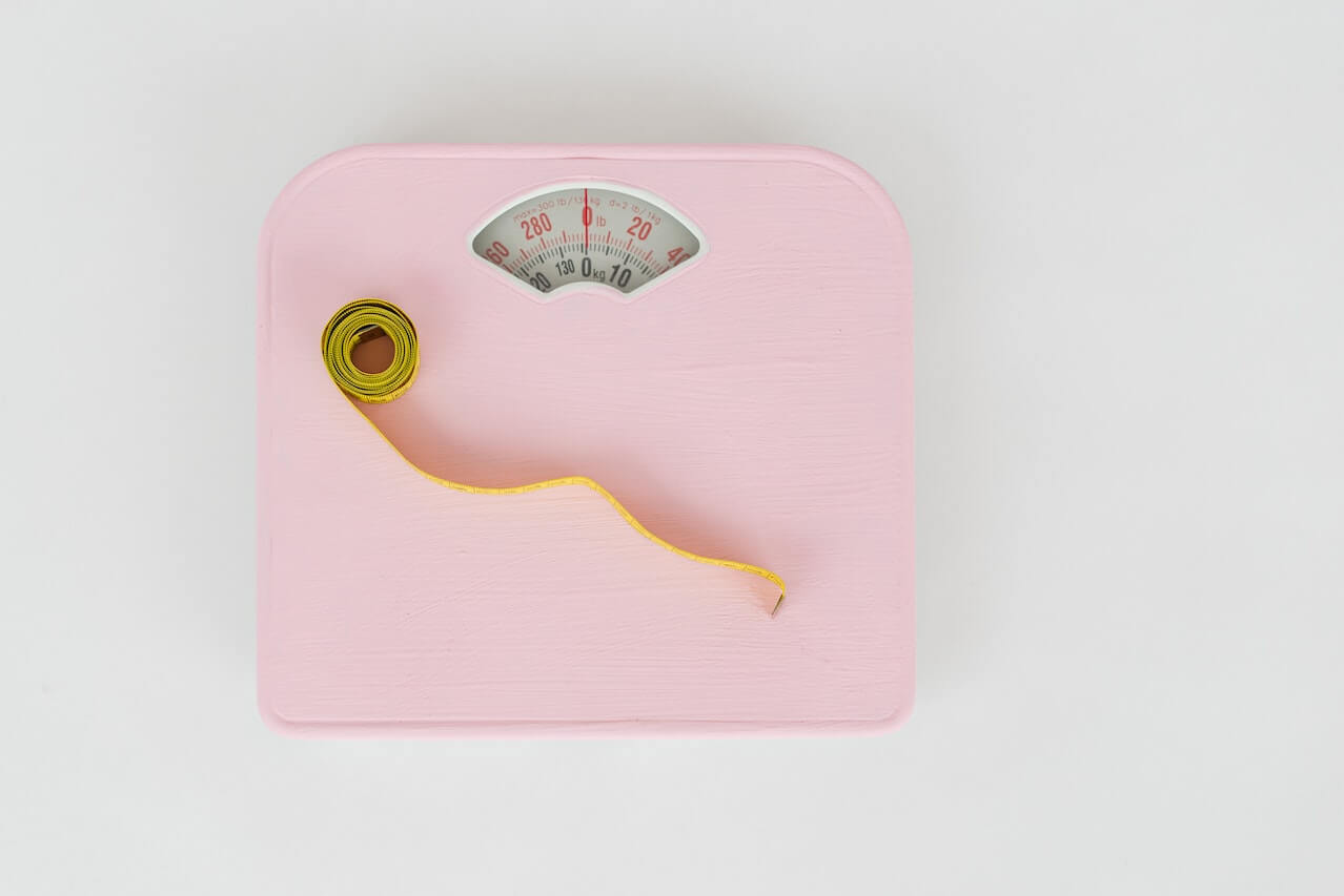 Pink bathroom scale with yellow measuring tape on white background