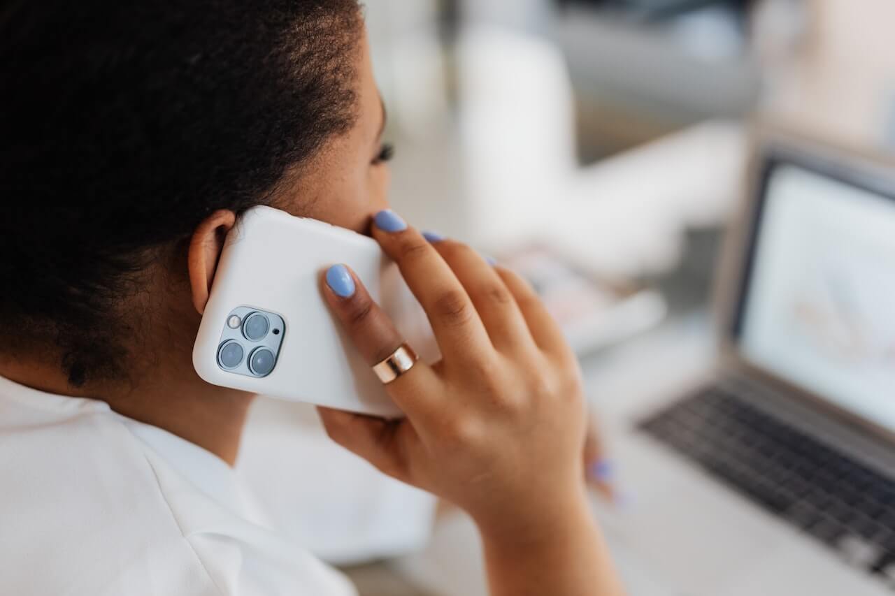Person with blue nails talking on white iPhone near laptop