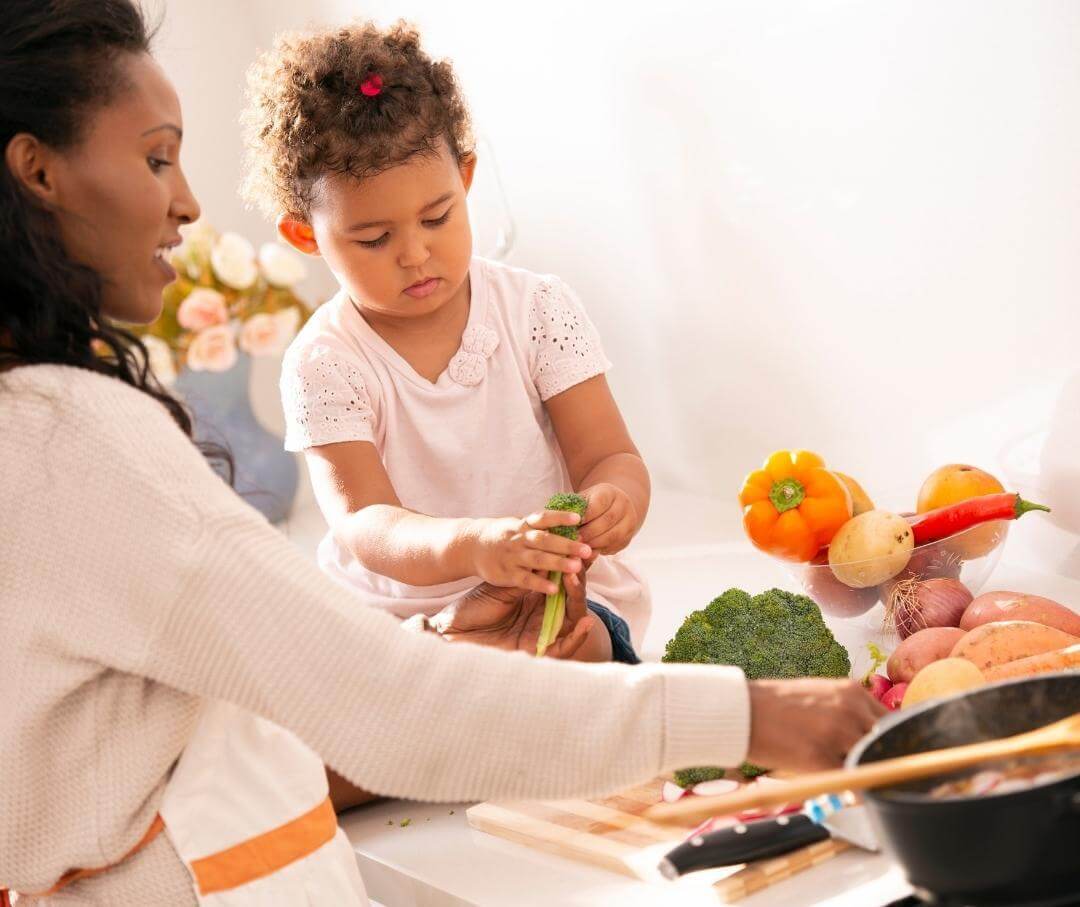 Young girl helps prepare vegetables in kitchen with adult