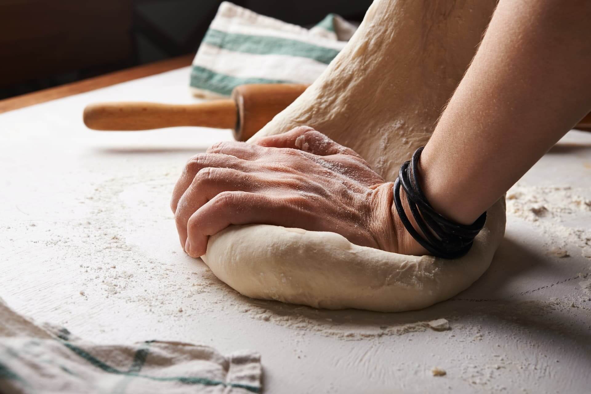 Hands kneading dough on floured surface with rolling pin and kitchen towel