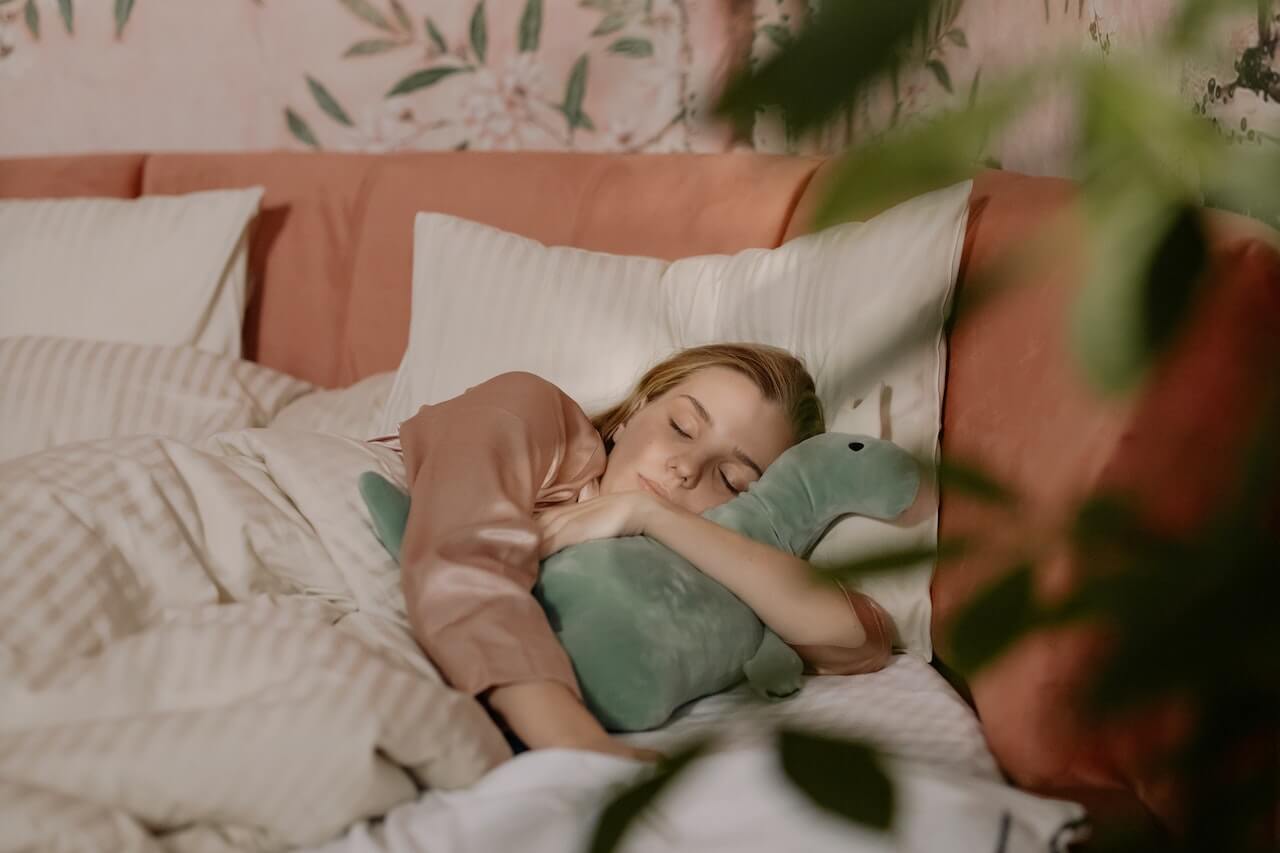 Person sleeping peacefully with green plush toy on cozy bed