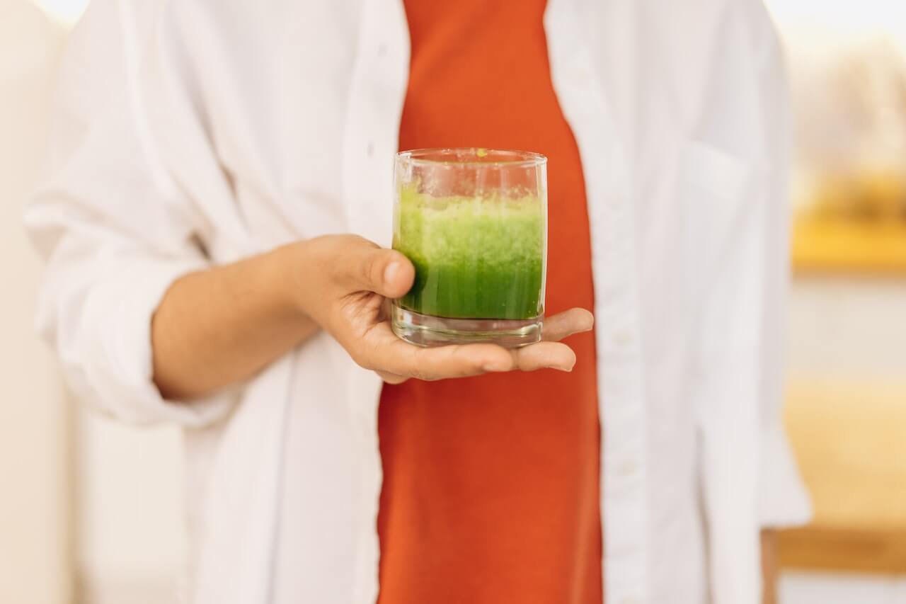 Hand holding fresh green juice in clear glass against white and orange background