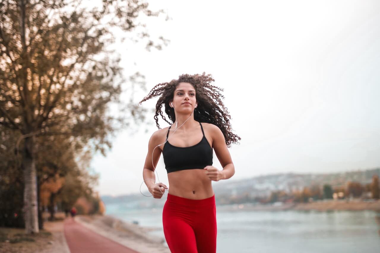 Woman running with curly hair on waterfront path during autumn