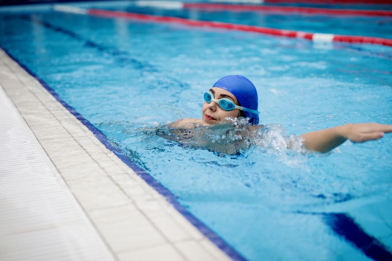 Swimmer in blue cap and goggles doing freestyle stroke in pool