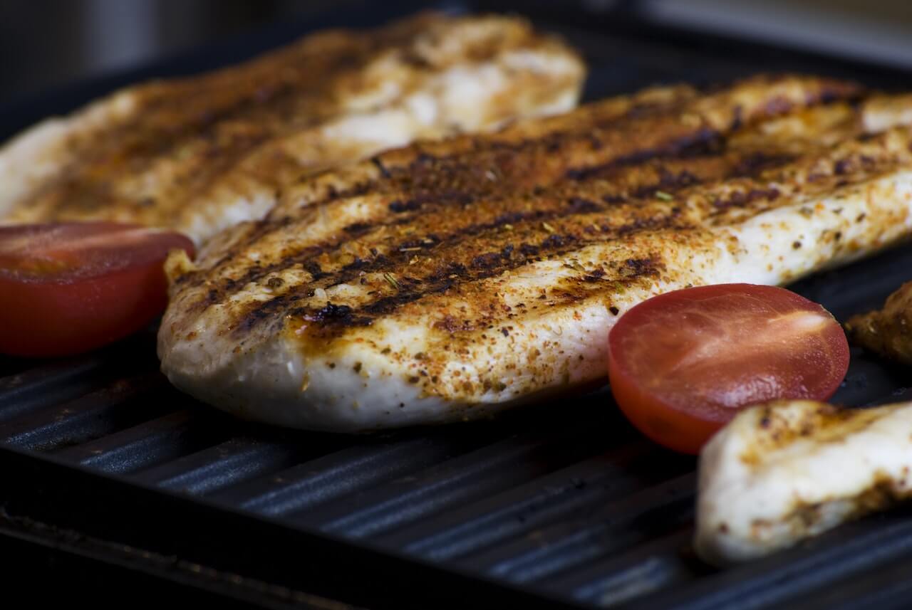 Grilled chicken breasts with grill marks, seasoned and served with tomatoes
