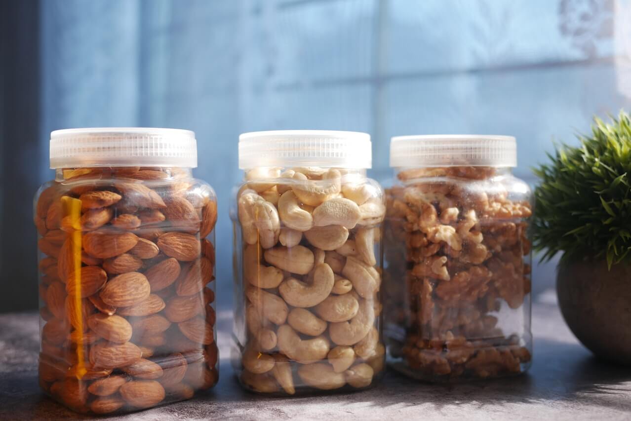 Three glass jars filled with different types of nuts on a blue background
