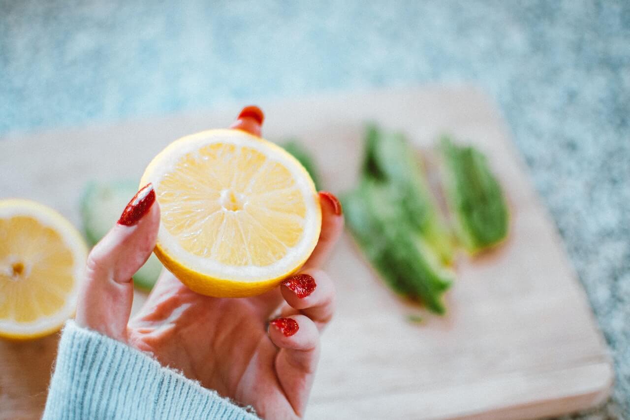 Hand with red nails holding a halved lemon on a wooden board