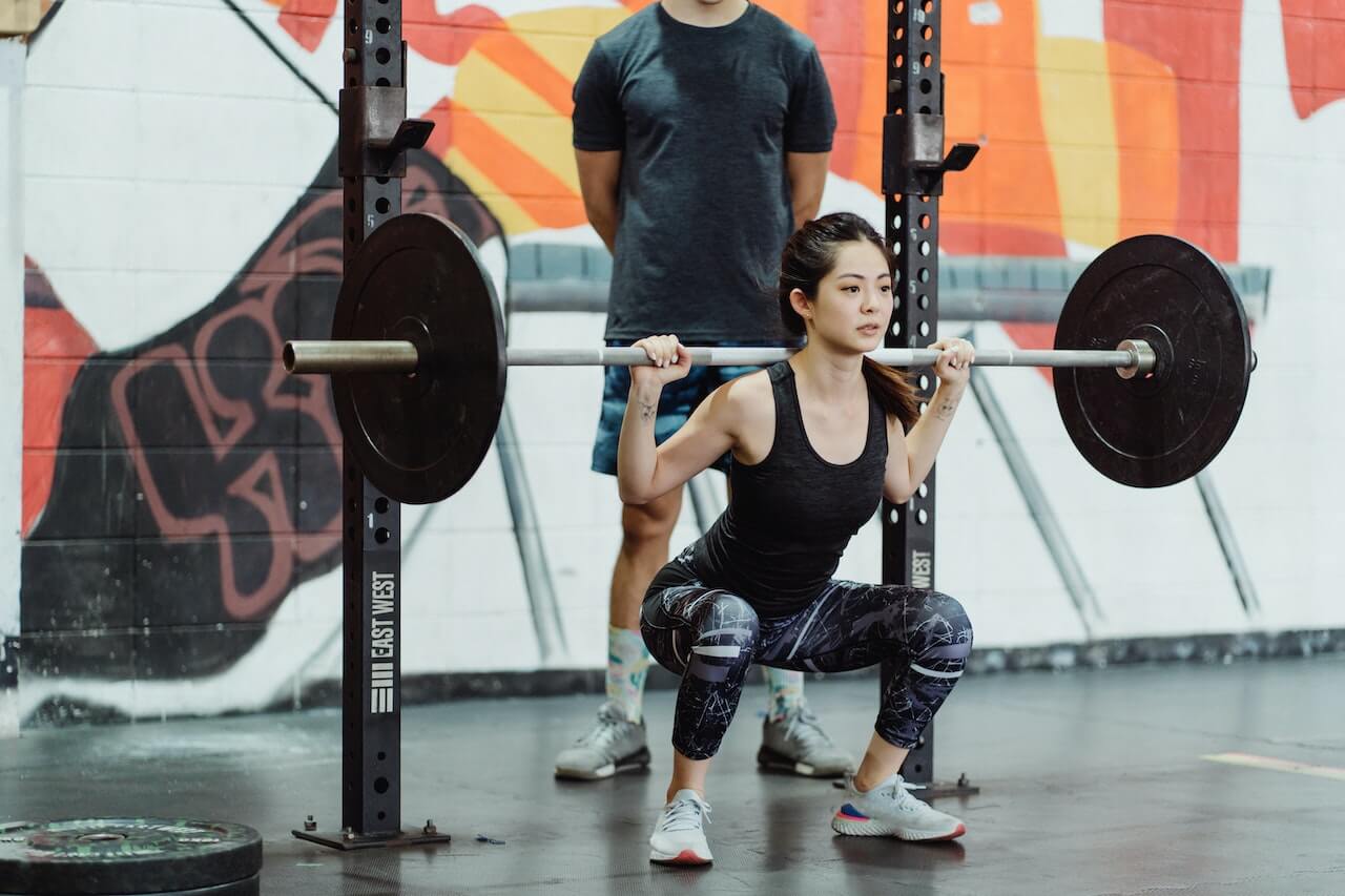 Woman performing barbell squat in gym with colorful wall behind