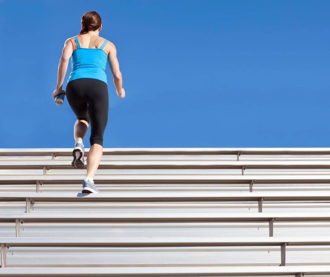 Runner in blue top climbing stadium bleachers against clear blue sky