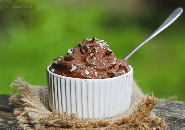 Creamy chocolate mousse in white ramekin with metal spoon, sprinkled with nuts