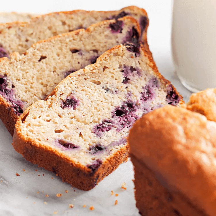 Sliced blueberry banana bread with fresh berries scattered throughout