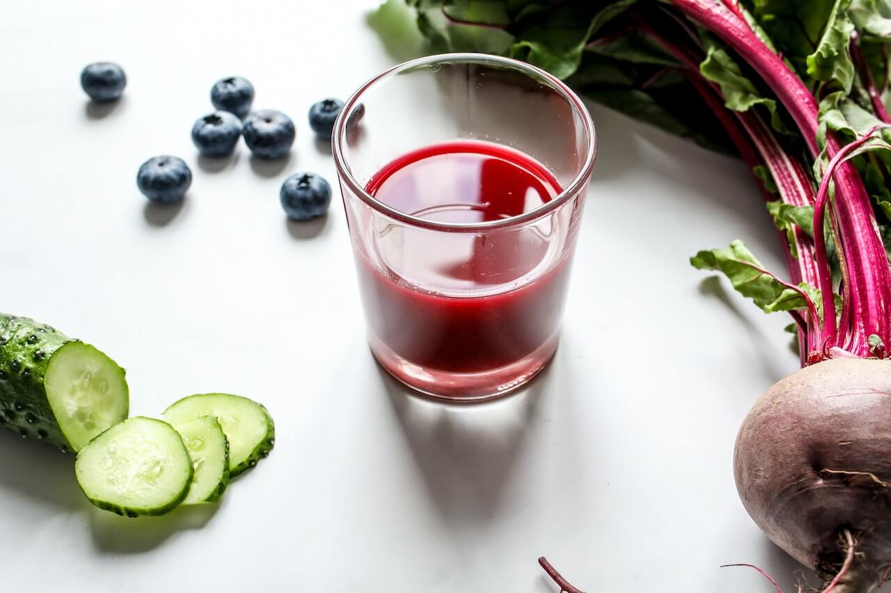 Red juice with blueberries, cucumber, and beetroot on white background