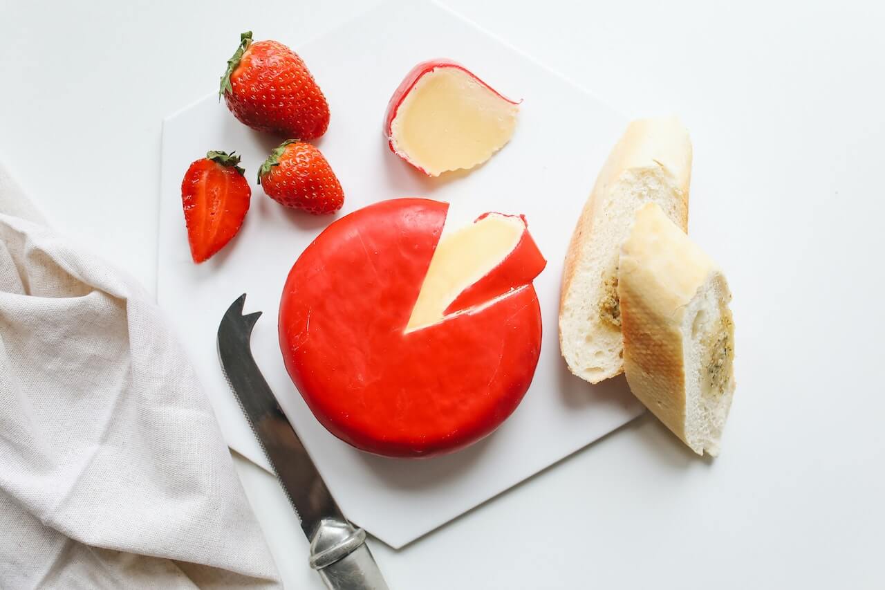 Fresh strawberries, red pepper spread with cheese, and bread sliced on white cutting board