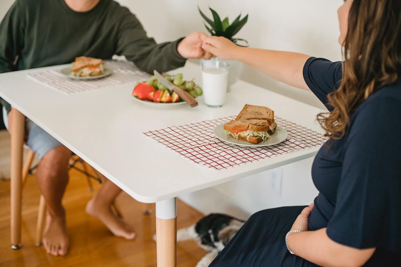 Two people sharing a meal at a table with sandwiches, vegetables, and drinks