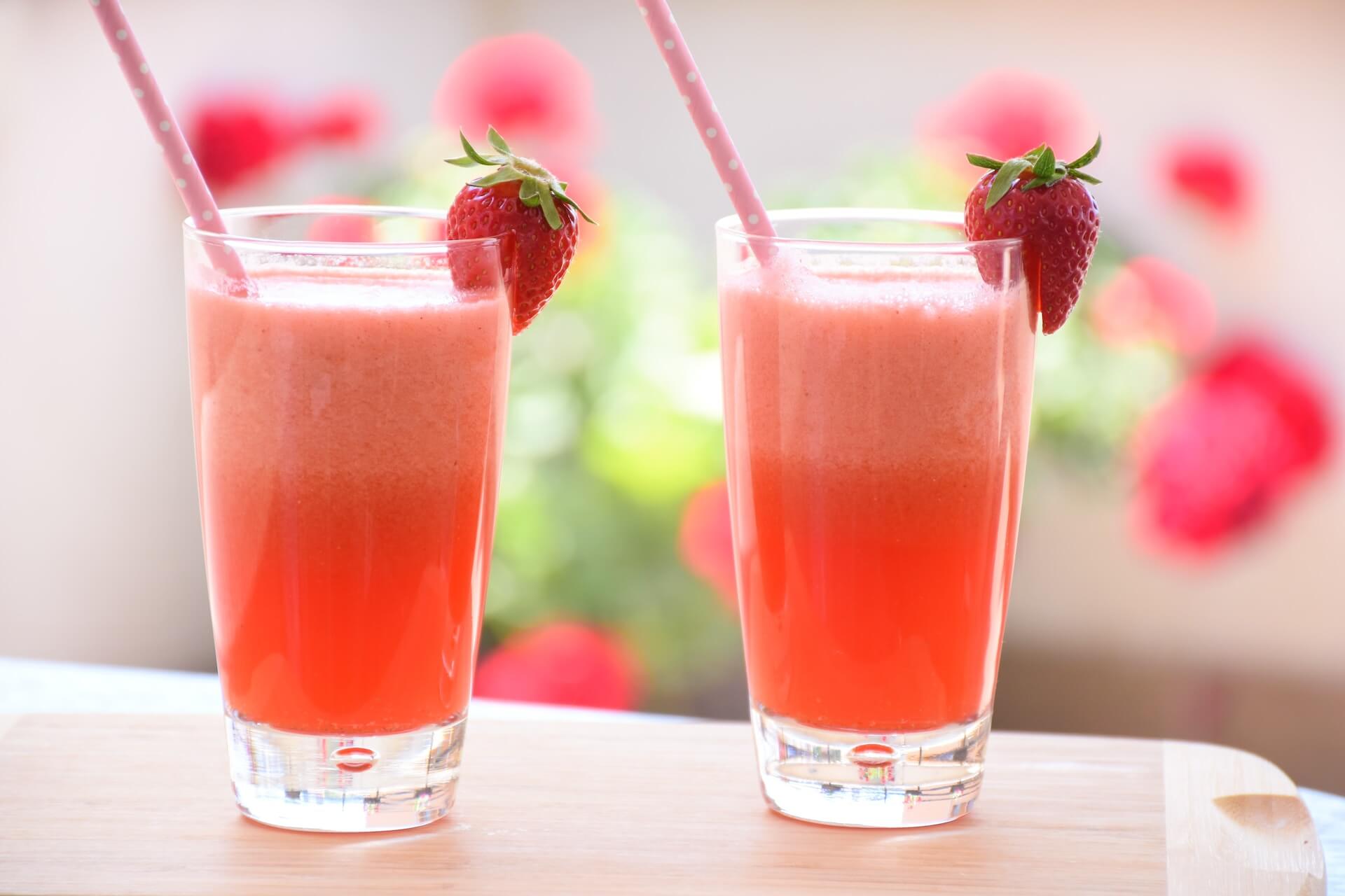 Two pink strawberry smoothies with fresh strawberries on wooden surface