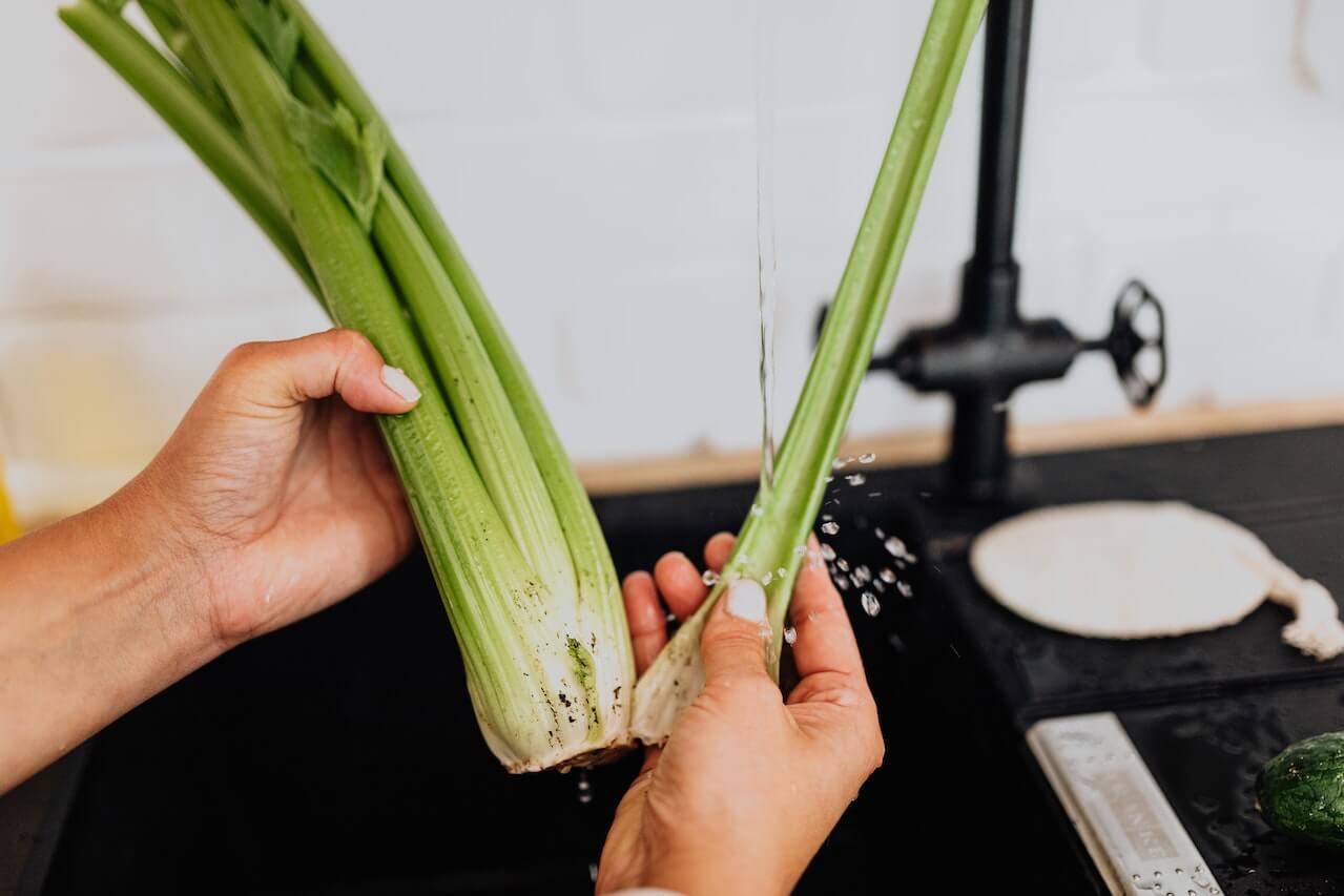 Hands rinsing leeks under running water at kitchen sink with faucet