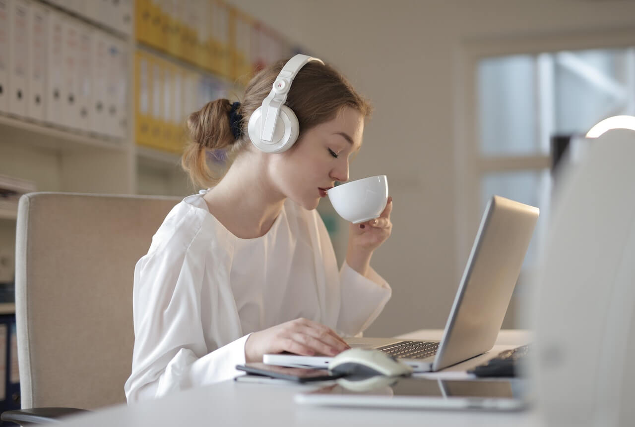 Woman drinking coffee while working on laptop with headphones