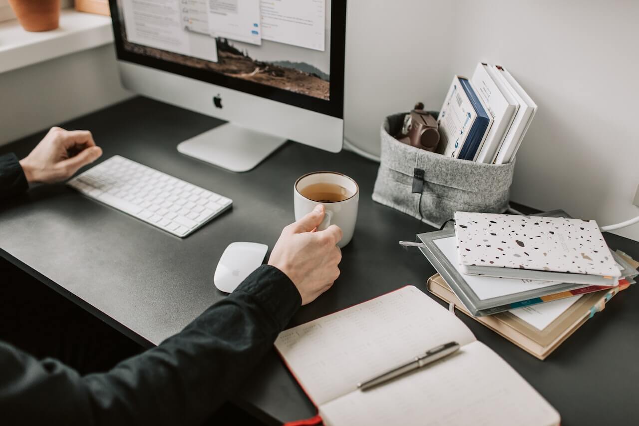 Workspace with iMac, coffee, books, and open notebook on dark desk