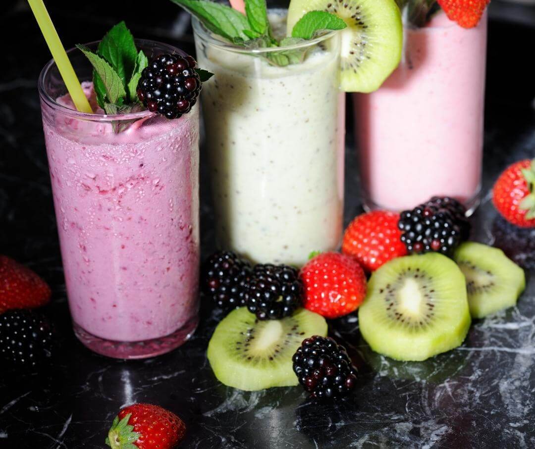 Colorful fruit smoothies with fresh berries, kiwi, and mint garnish