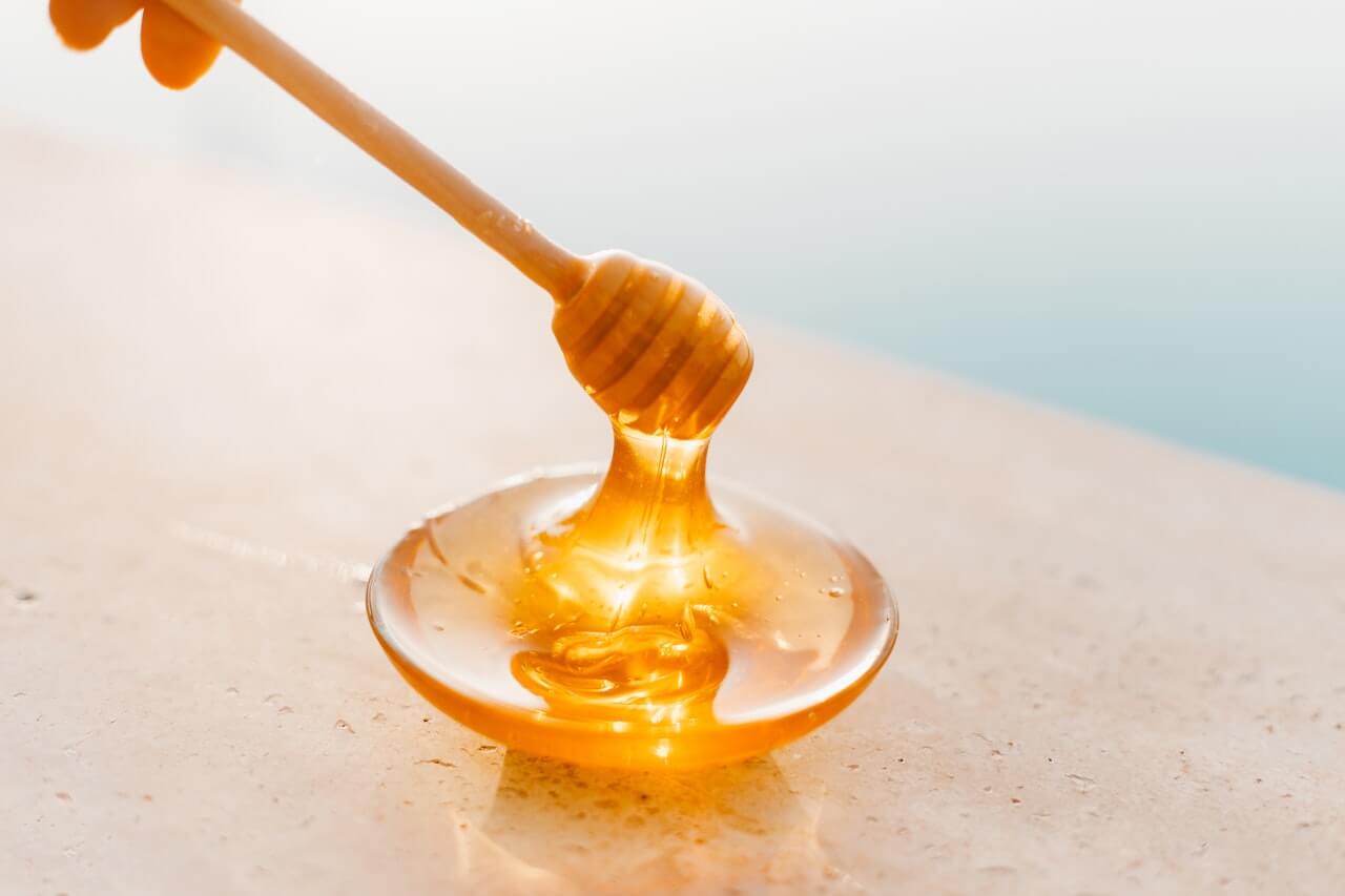 Golden honey dripping from wooden dipper onto glass surface