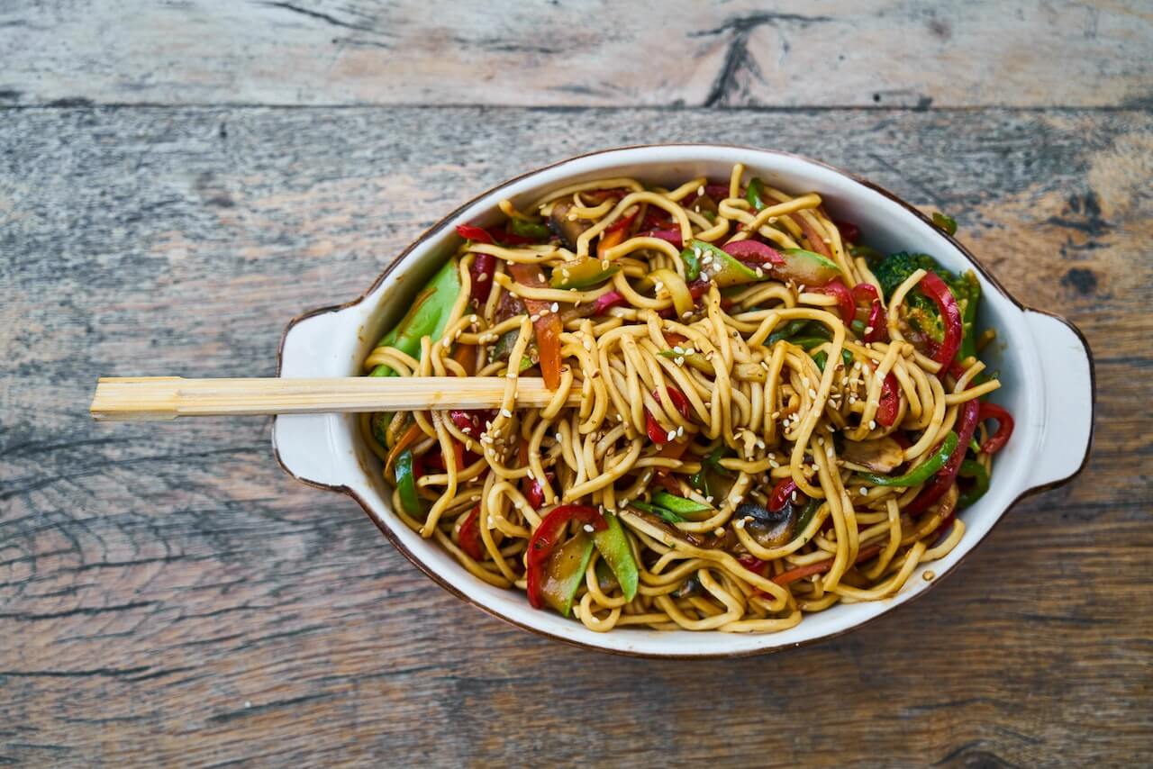 Colorful vegetable noodles with chopsticks in white ceramic dish