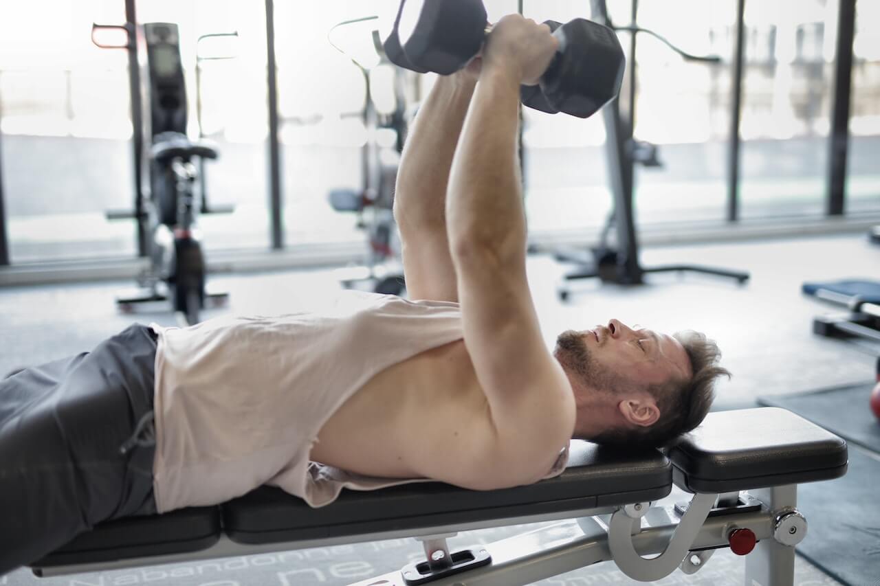 Man lifting dumbbell while lying on bench in fitness gym