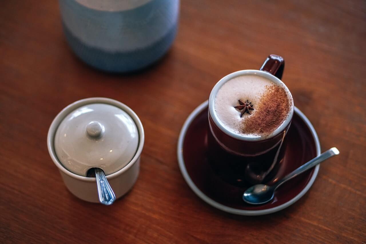 Spiced coffee with star anise garnish beside a sugar container on wooden table