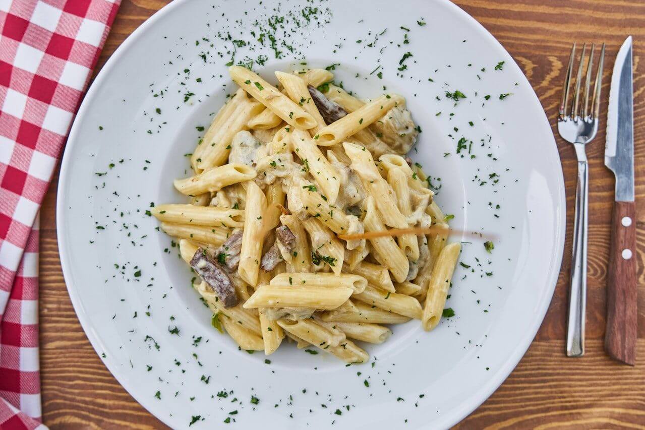 Creamy penne pasta with herbs sprinkled on top, served on white plate