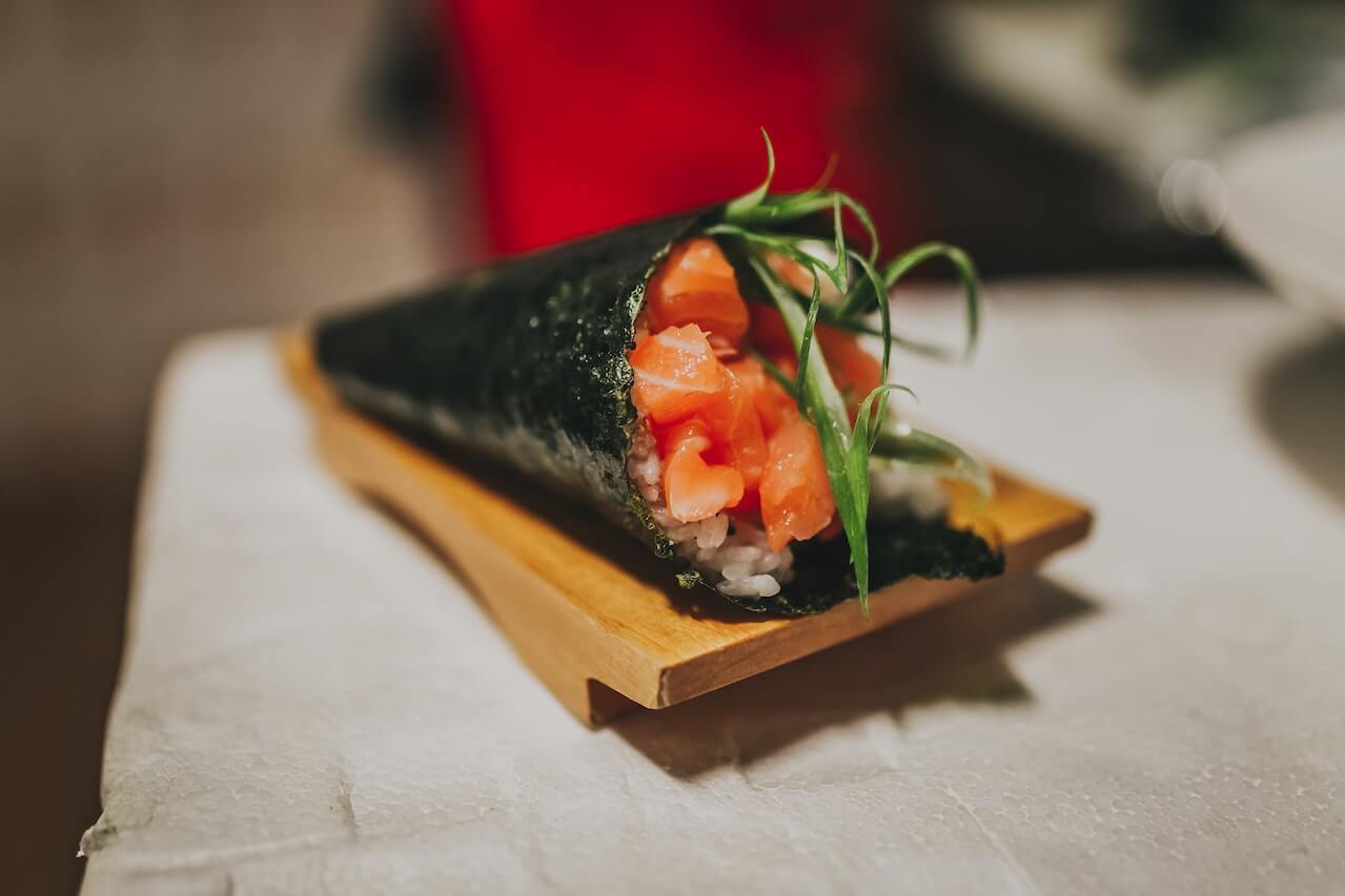 Salmon temaki sushi hand roll with fresh herbs on wooden board