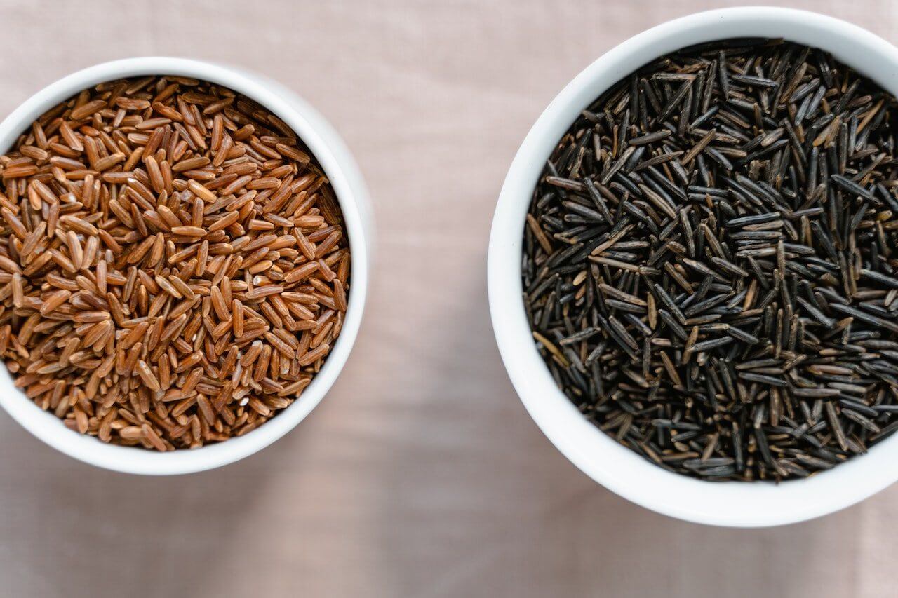 Two white bowls of brown and black rice varieties