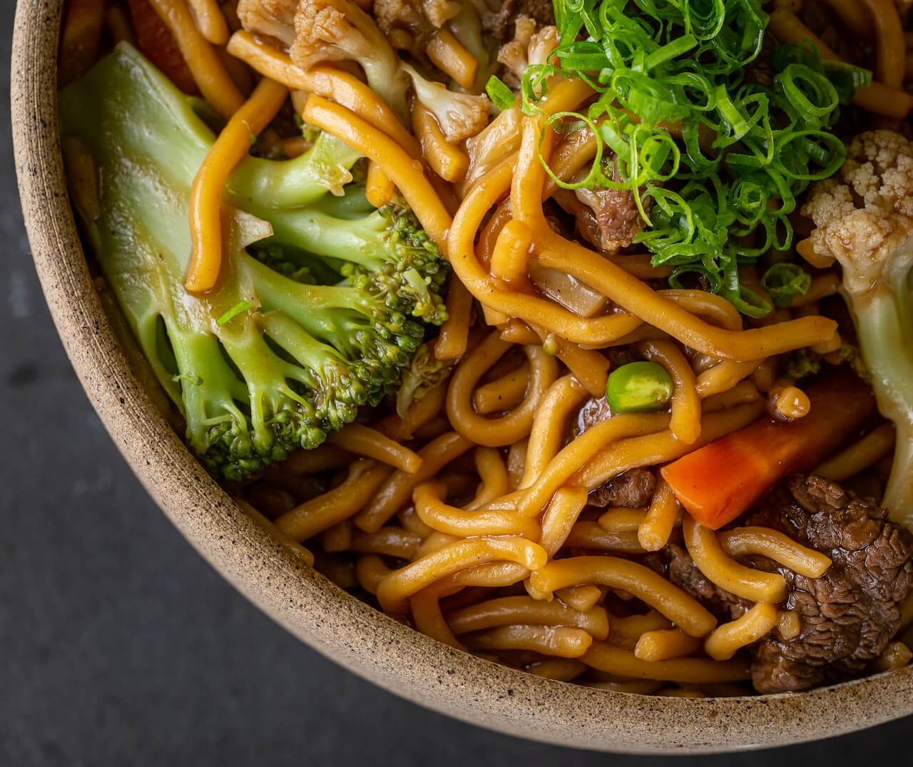 Beef noodle stir-fry with broccoli and green onions in ceramic bowl