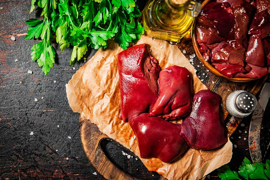 Fresh raw beef liver on wooden board with olive oil, salt, and fresh parsley herbs