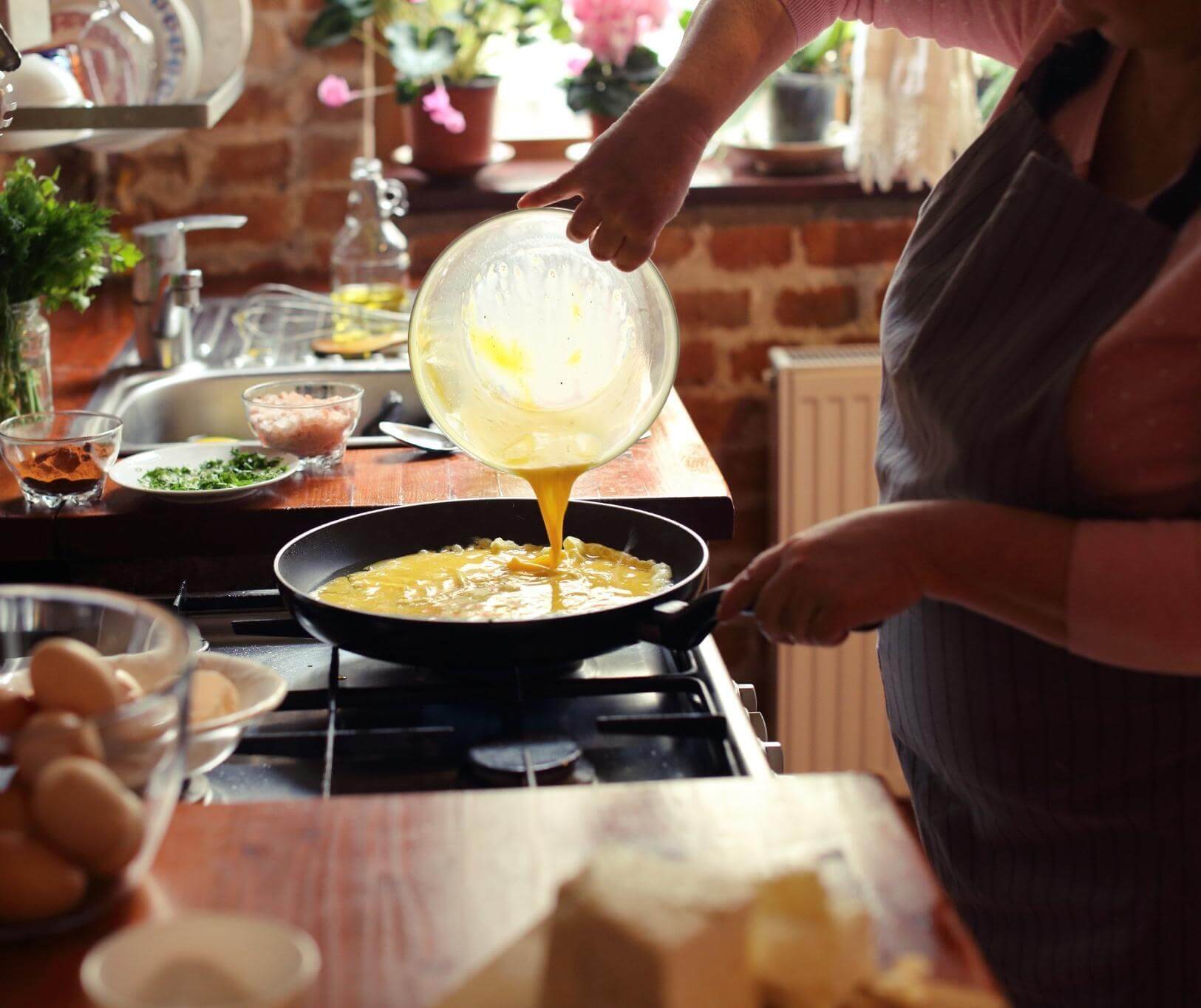 Person pouring omelet from pan into skillet on stovetop in kitchen