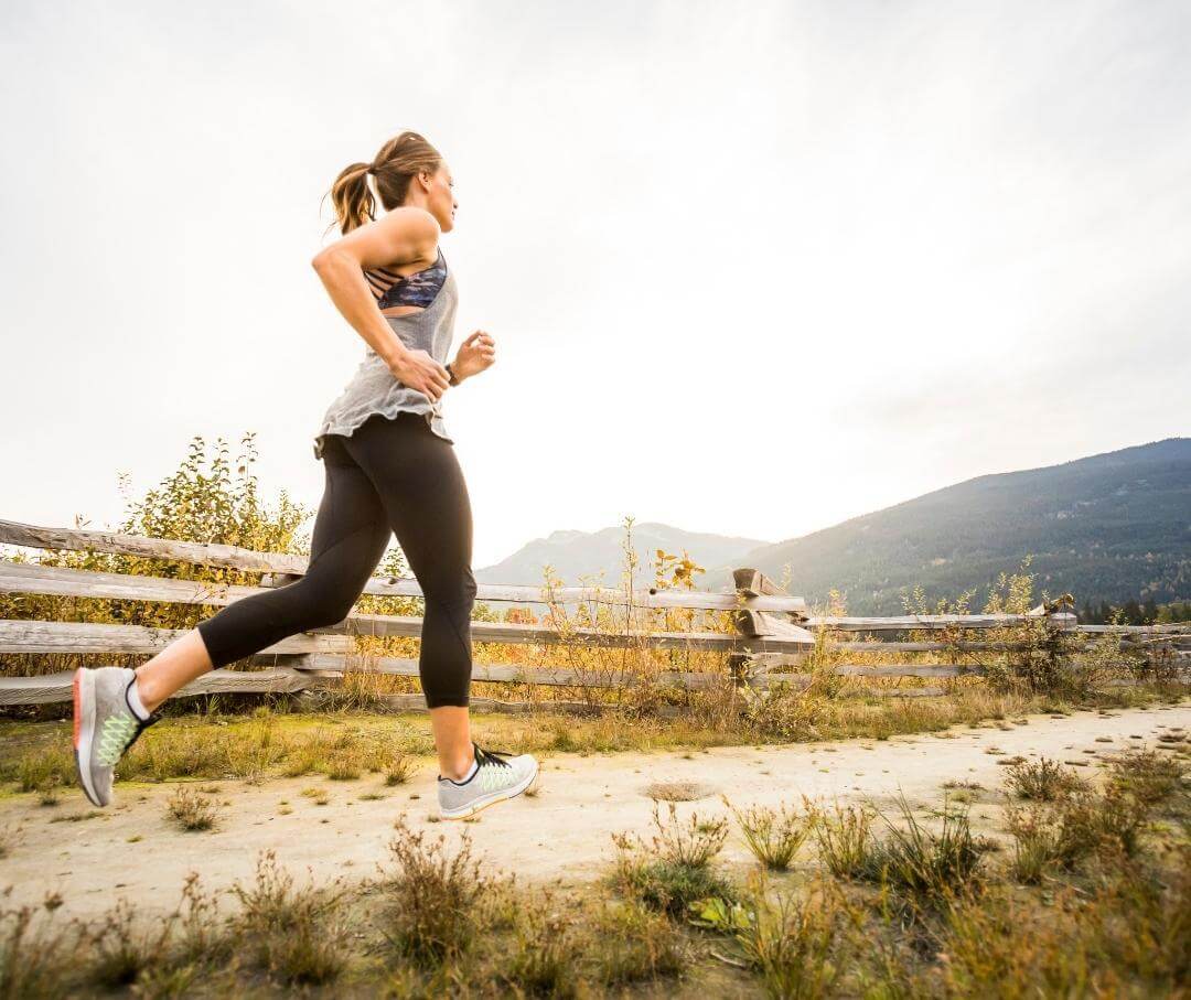 Runner jogging on mountain trail with wooden fence and autumn landscape