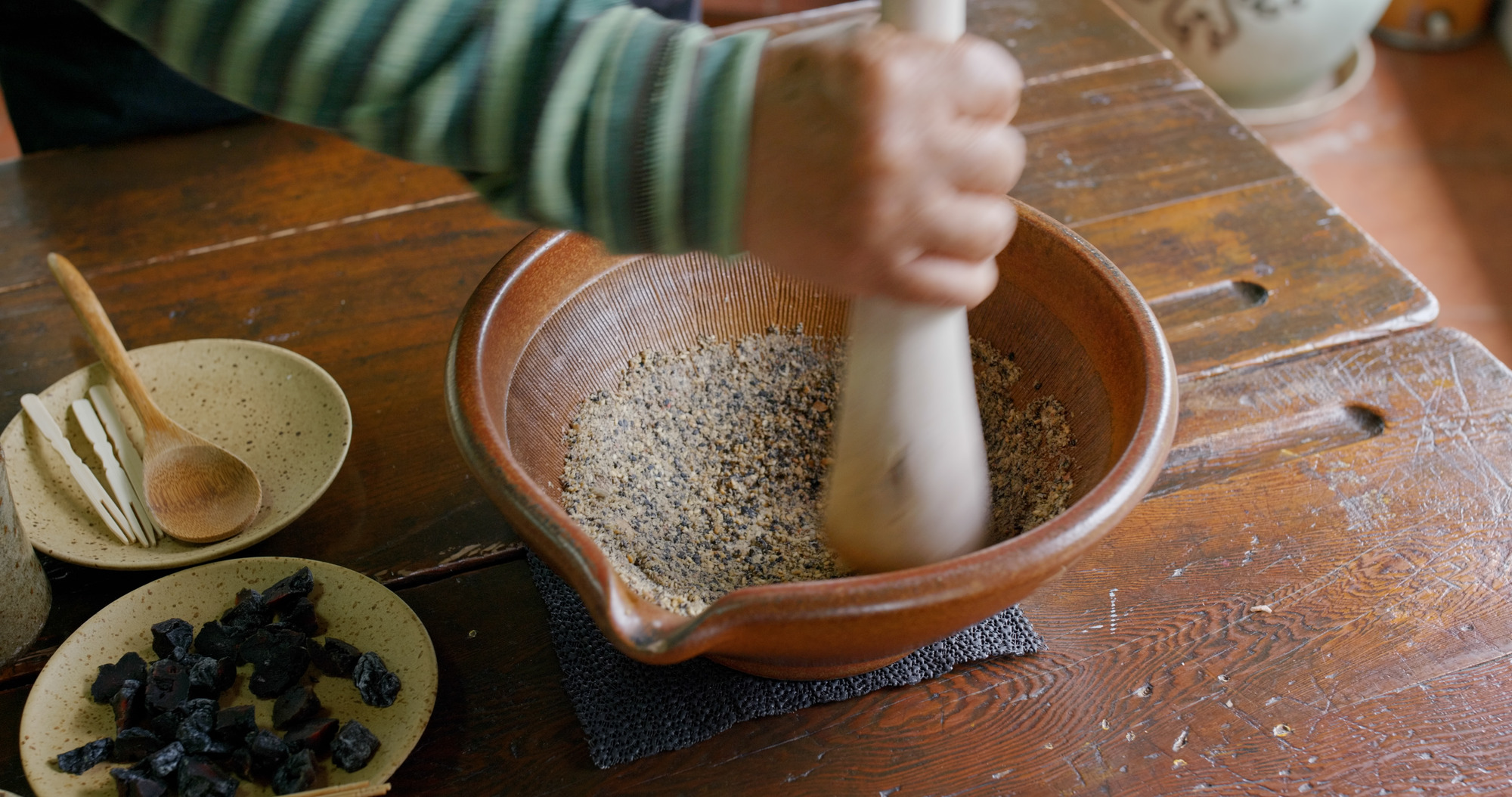 Hand grinding spices in ceramic mortar with pestle on wooden table