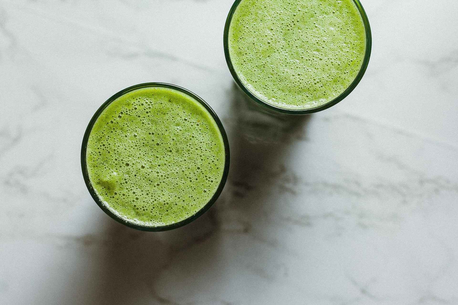 Two glasses of vibrant green smoothie with foam on a marble surface
