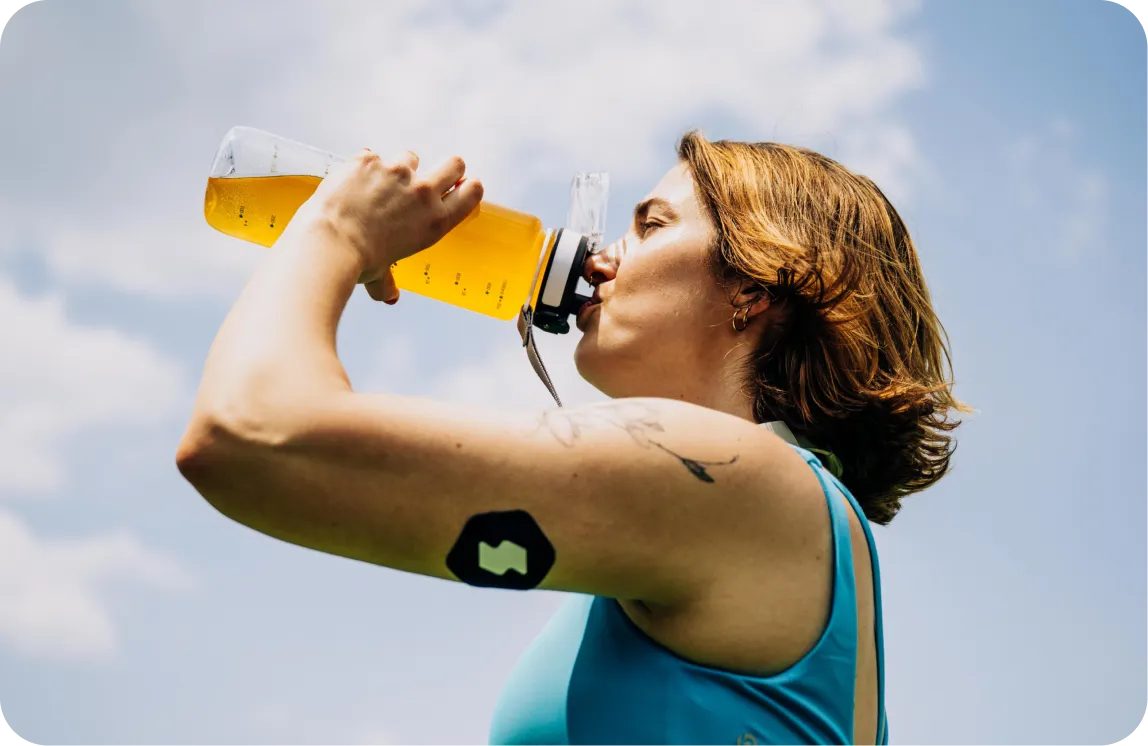 Person in blue tank top drinking from yellow sports water bottle outdoors