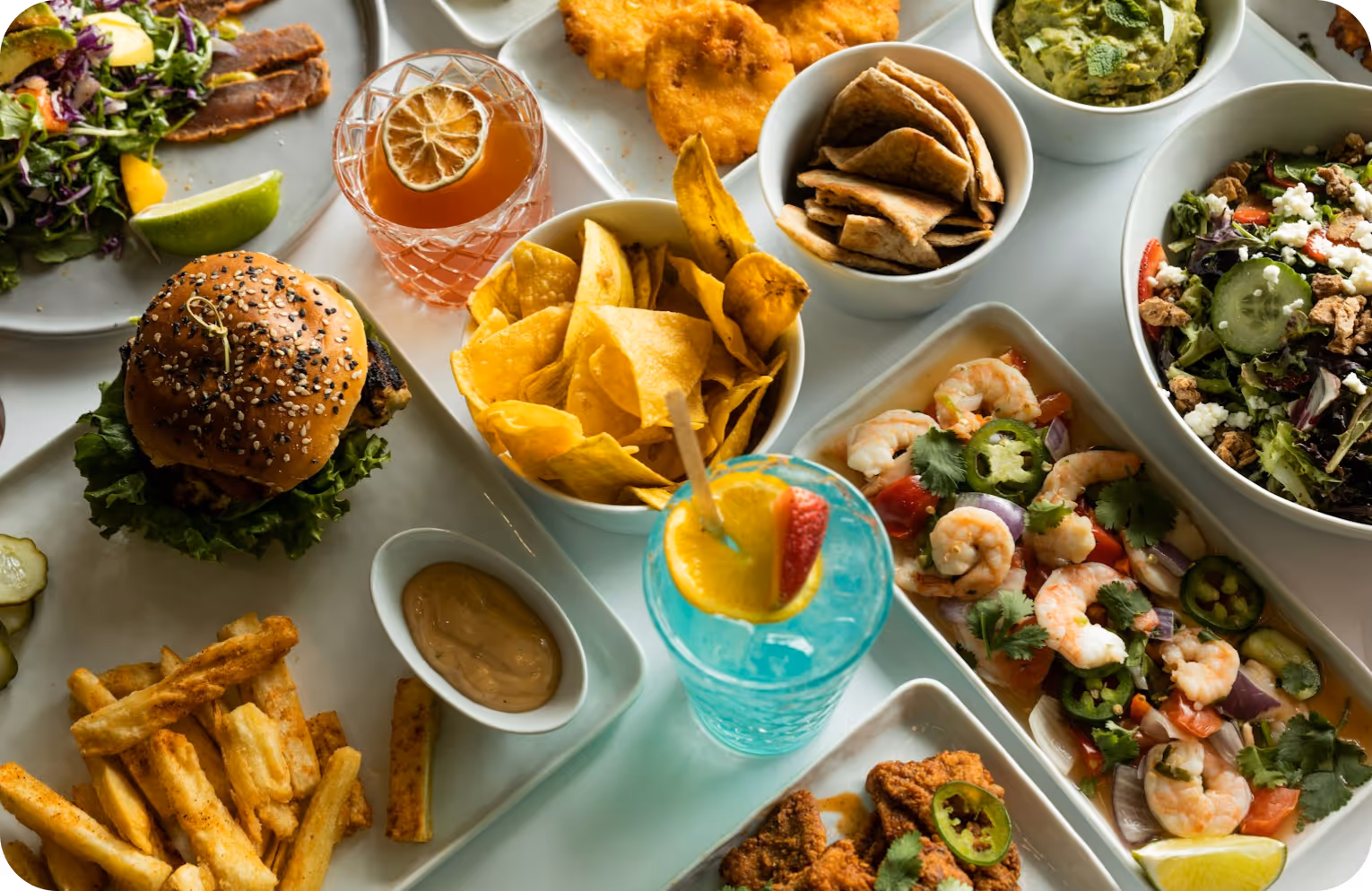 Colorful spread of burgers, chips, shrimp, cocktails, and salads on white plates