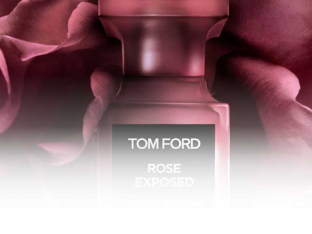 A Tom Ford "Rose Exposed" perfume bottle (50 ml eau de parfum) and lipstick with a black cap with the "TF" emblem, as well as an eye shadow palette set on a pink rose petal or fabric background.Image from Plural, NYC - Social Media Marketing & Content.