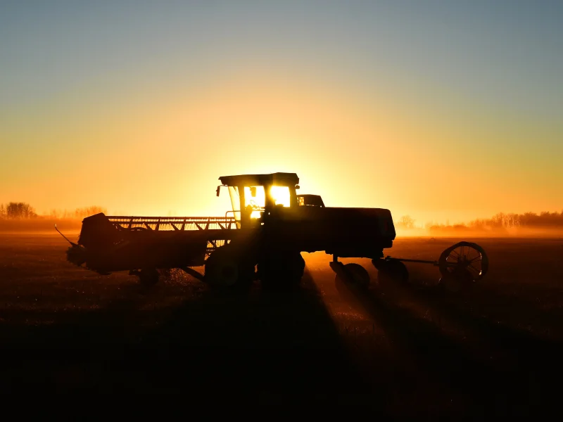 Farm equipment financing for tractor and harvester at sunrise in Canadian agricultural field