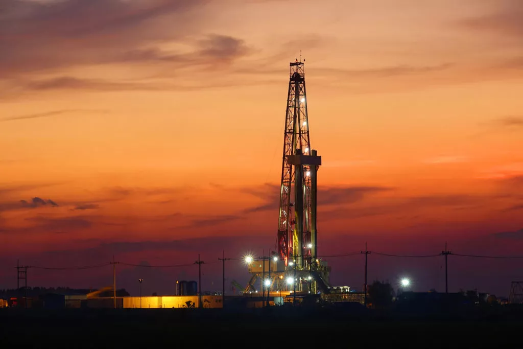 A rig in the desert over an orange sunset.