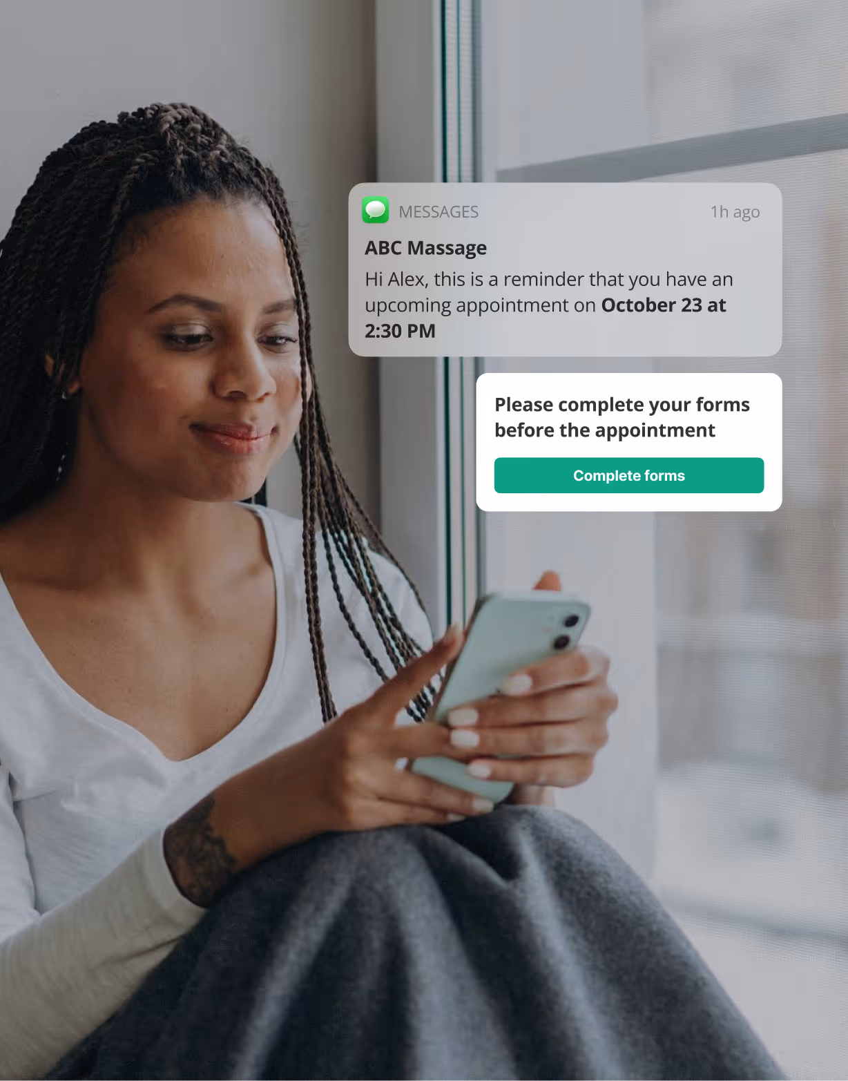 Woman sitting by a window looking at her phone with a massage appointment reminder and a prompt to complete forms before the appointment.